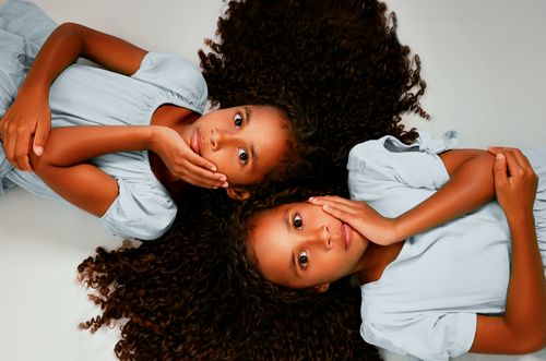 Free Charming portrait of twin sisters lying together, showcasing their bond and beauty. Stock Photo
