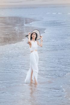 A woman in a white dress and hat walks gracefully along the beach, capturing a serene summer vibe.