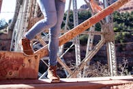 特写镜头中，一个穿着牛仔裤和靴子的人正穿过塞多纳阳光下的一座生锈铁桥