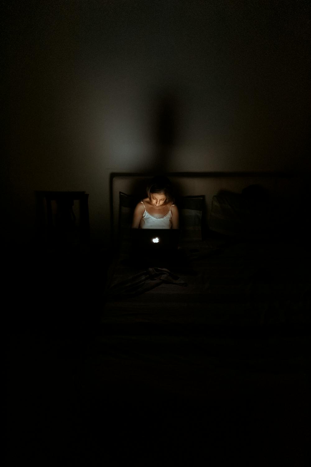Image of a woman facing her Macbook in the dark whilst in bed 