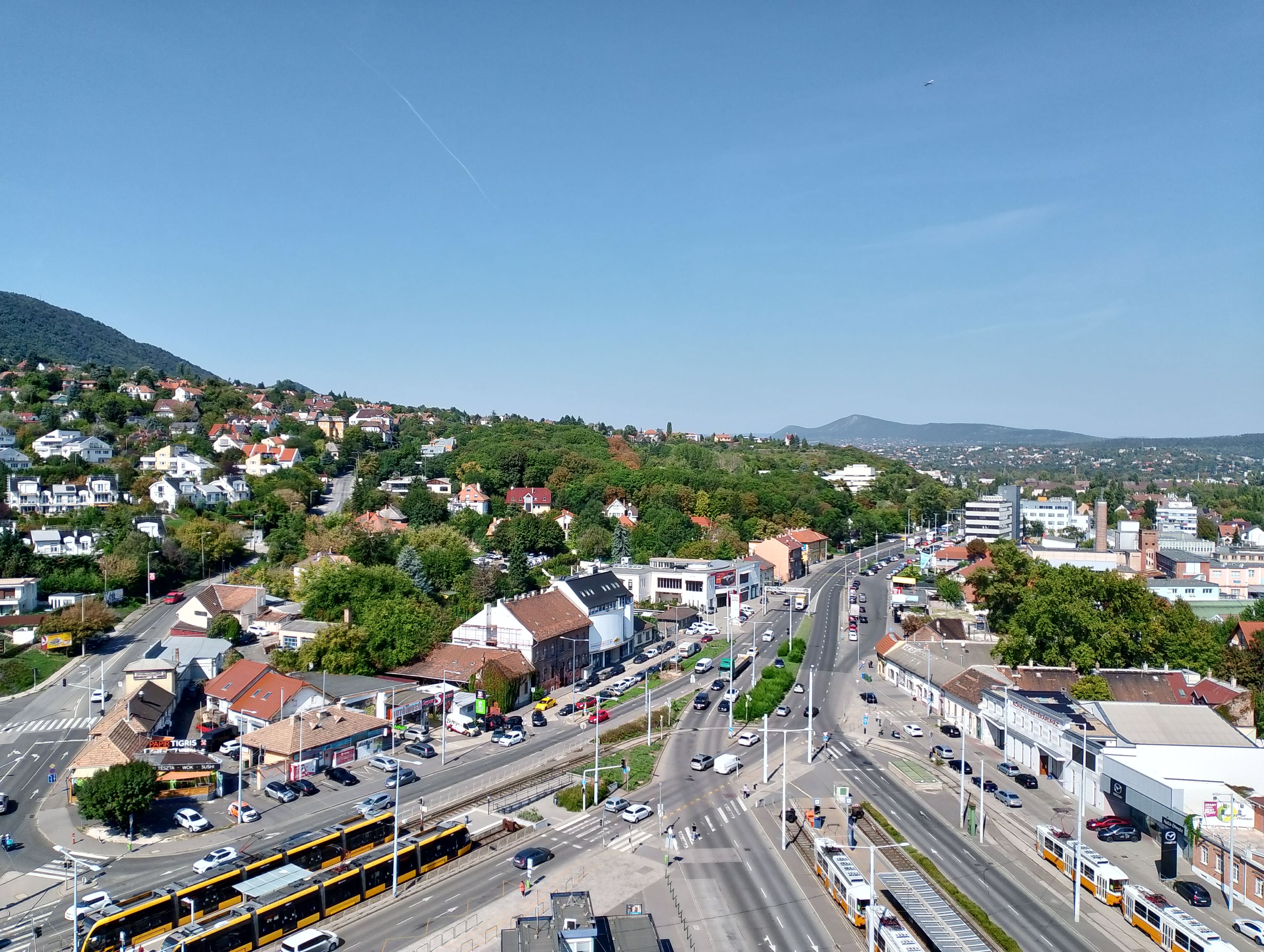 Aerial shot of a suburban landscape featuring housing, roads, and a tram in a sunny cityscape.