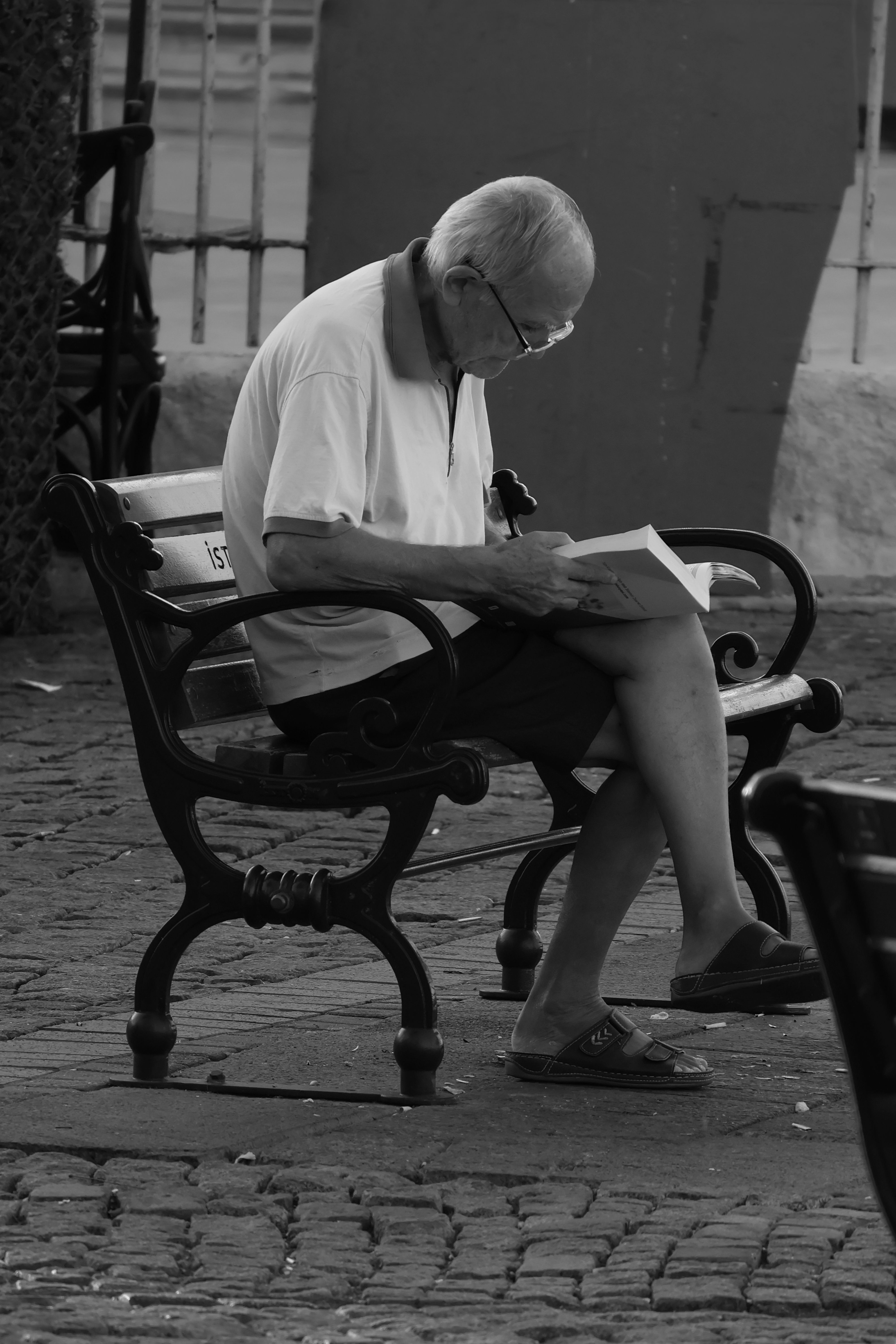 Black and white photo of an elderly man reading on a bench in Istanbul.