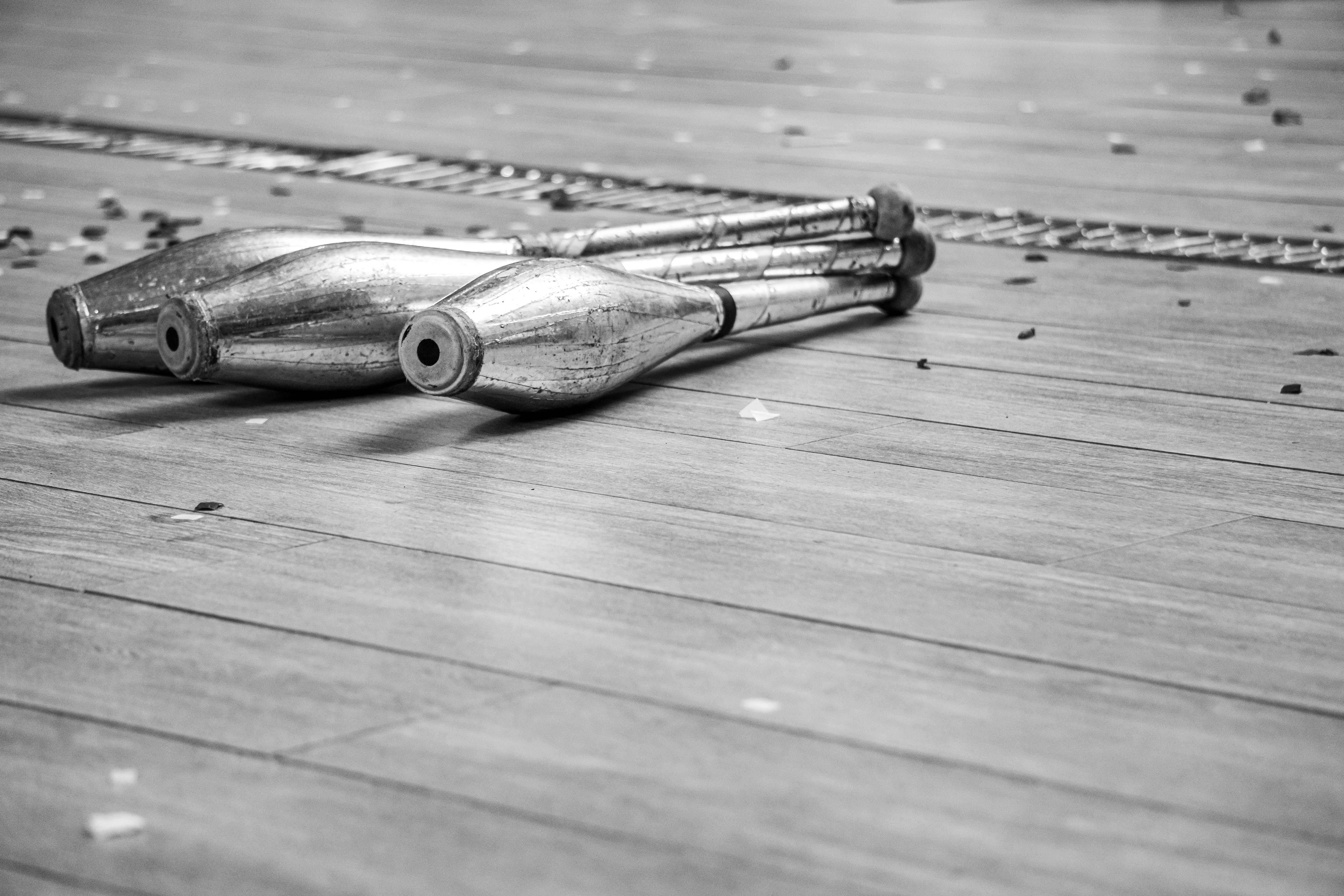 Monochrome image of juggling clubs resting on a wooden floor after a performance.