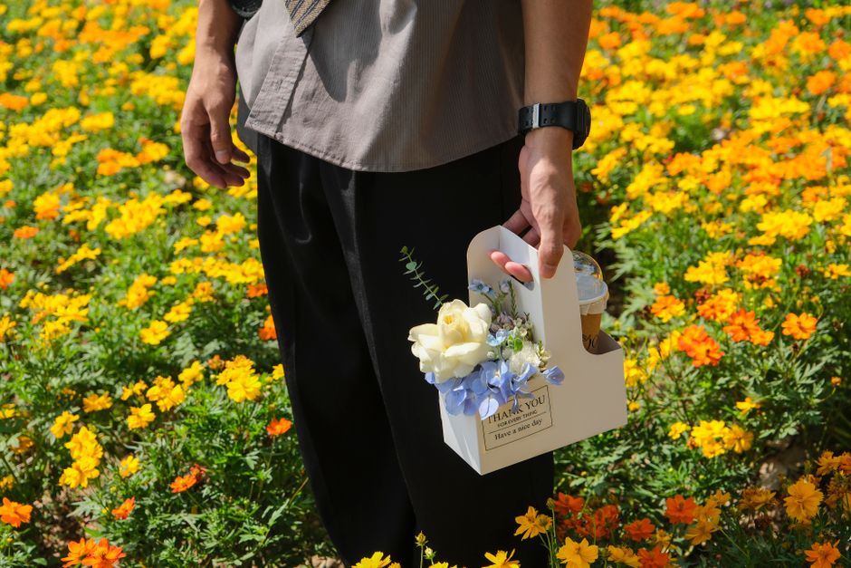 A man holds a basket with flowers and drink in a vibrant flower field.