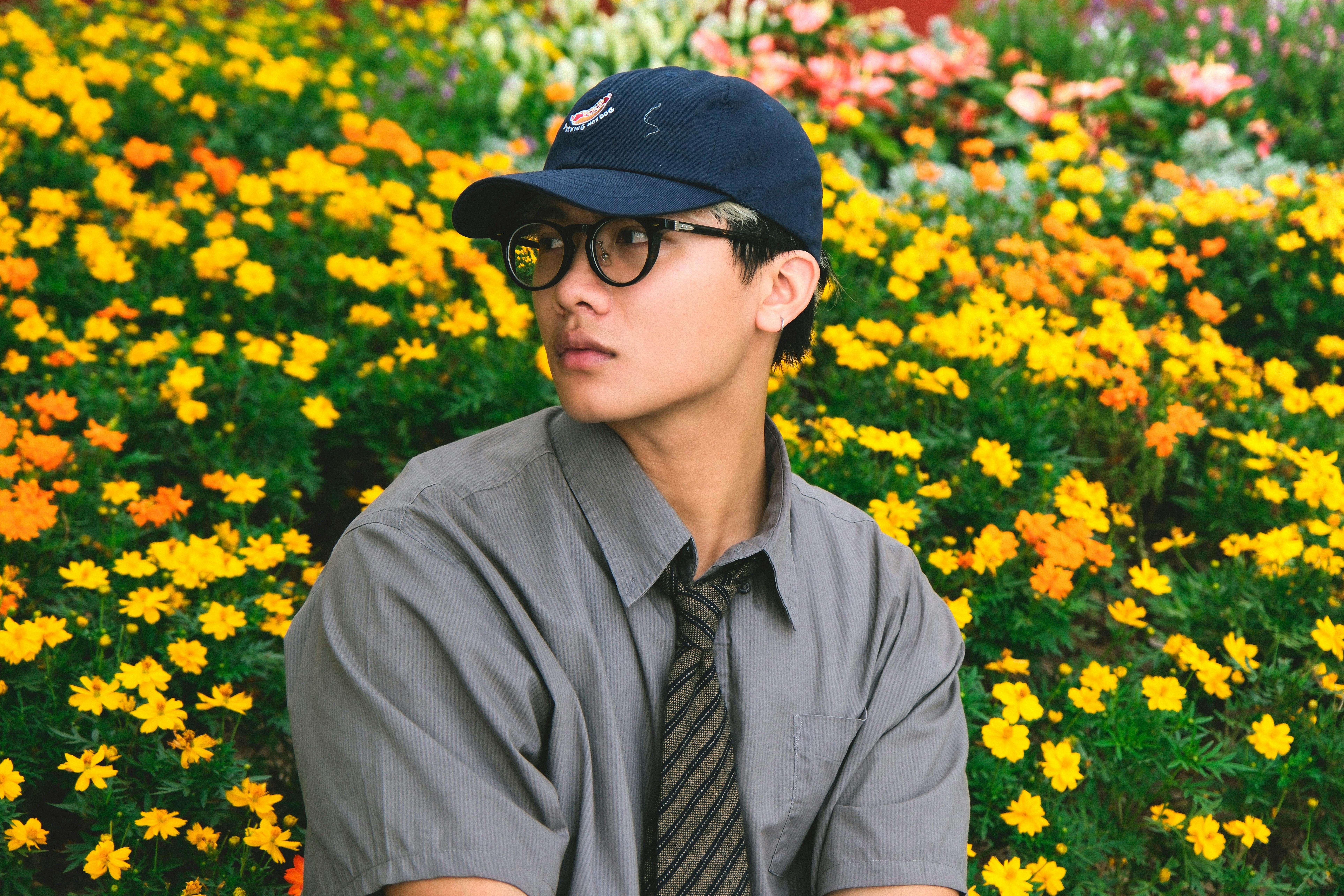 Kostnadsfria Ung Vuxen I Mössa Nära Den Pulserande Blomsterträdgården Stock foto