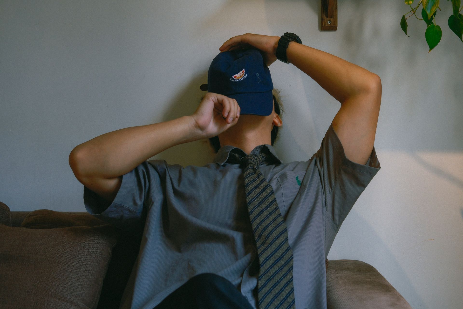 Person in casual attire with cap reclines on couch in relaxed pose, indoors.