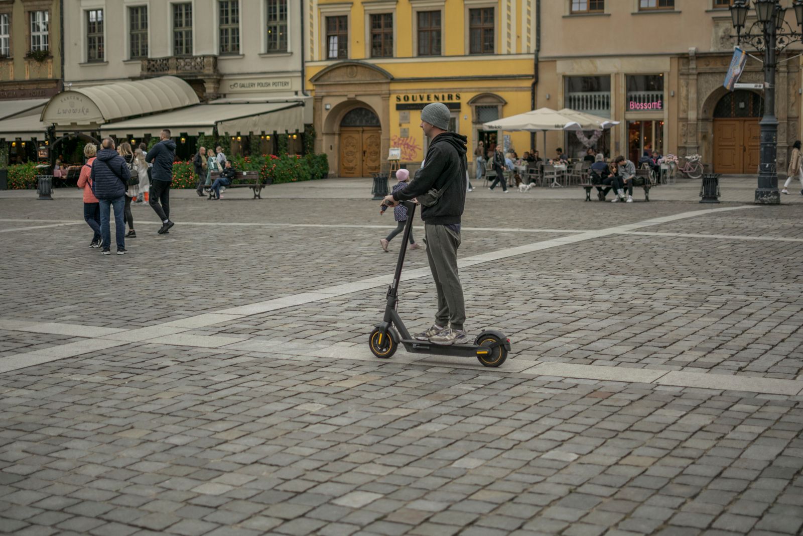 A rider using a shared e-scooter through a busy city square, illustrating real-world micro-mobility demand