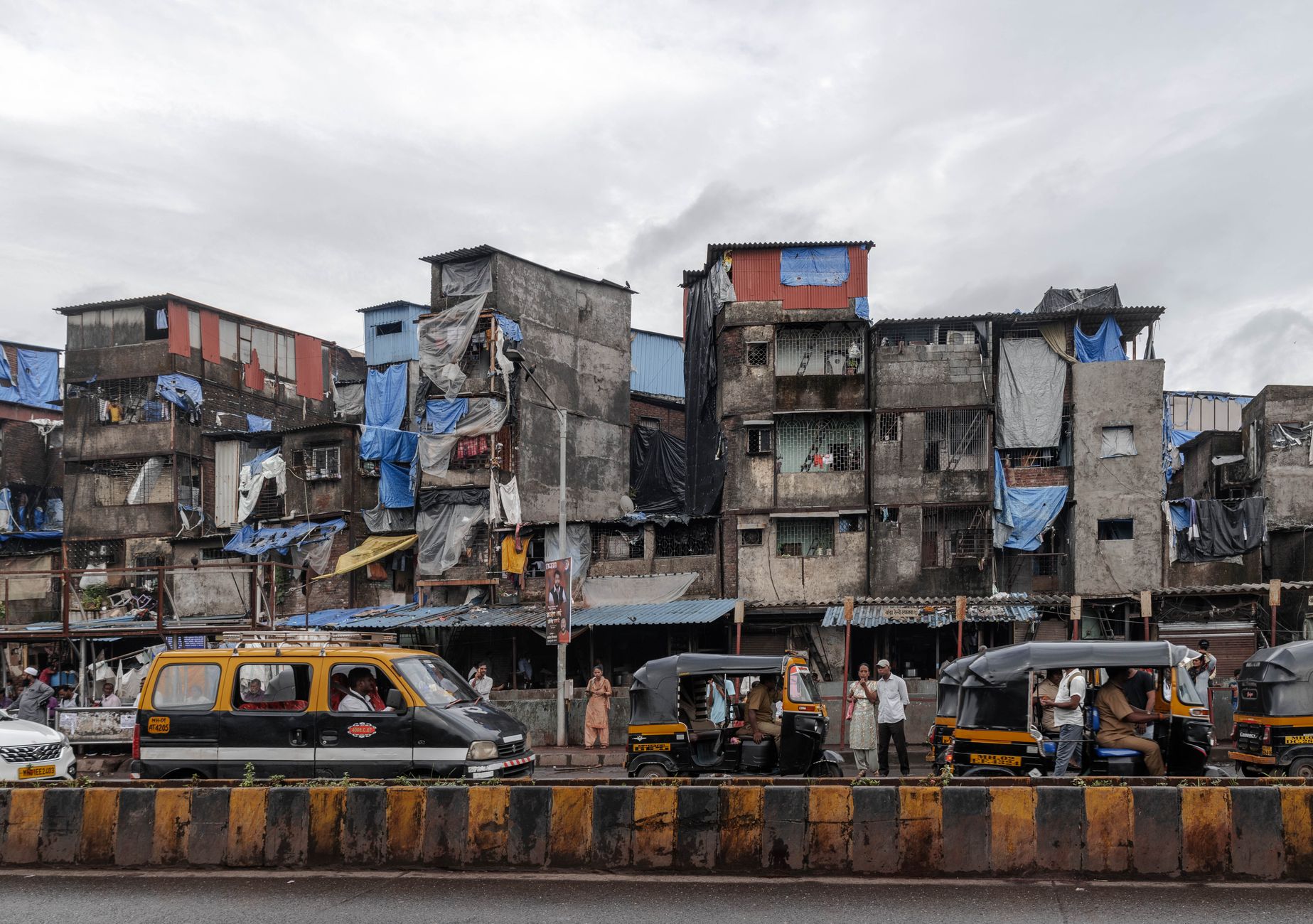 Street scene in Mumbai, showcasing auto rickshaws and residential buildings on a cloudy day.