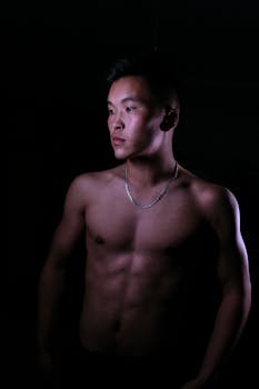 A powerful low-light portrait of a shirtless male model showcasing his physique.
