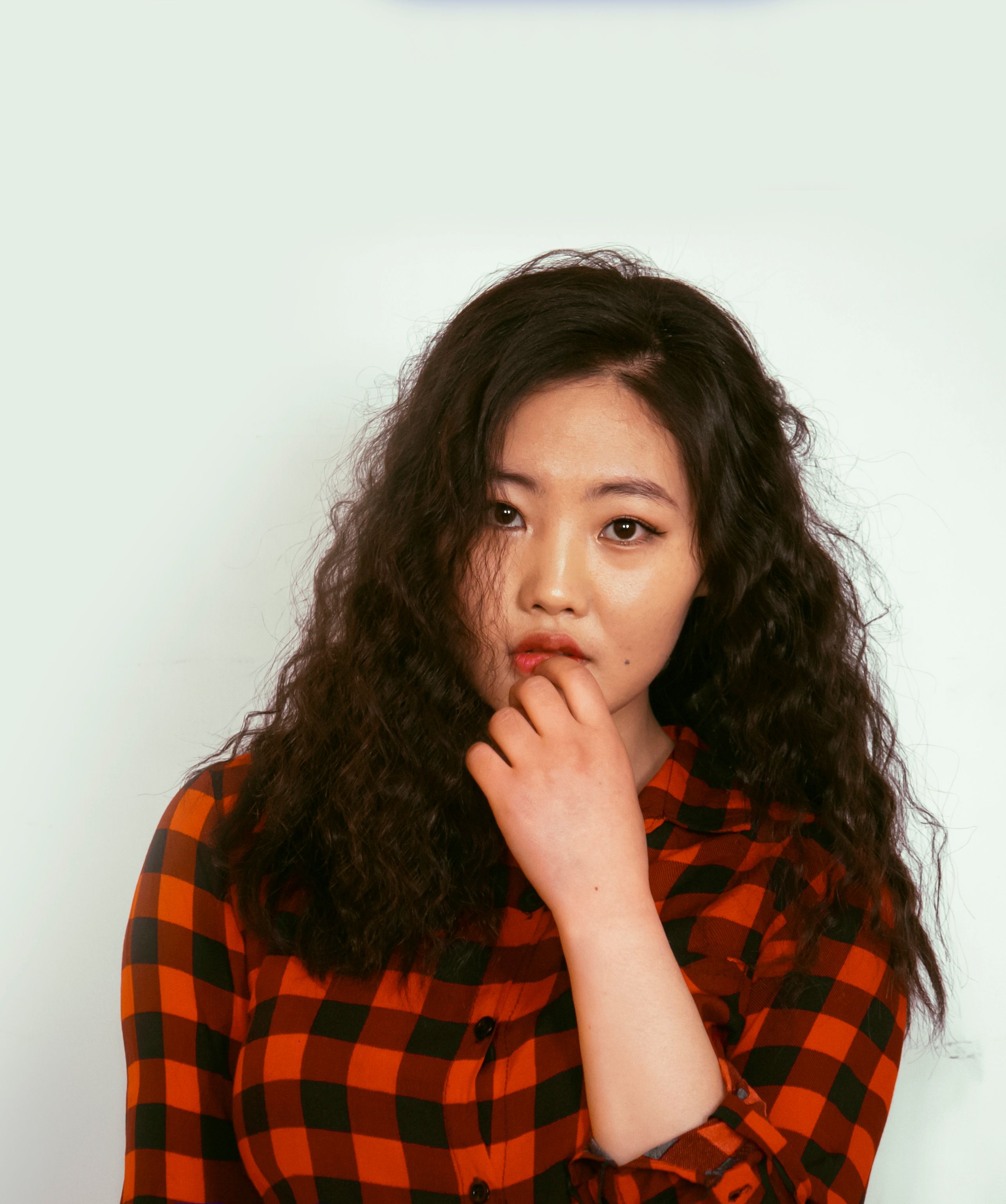 Portrait of a thoughtful woman in a red plaid shirt with a neutral background.