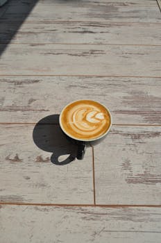 阳光洒在质朴的木制桌面上，一杯精美的拿铁与拉花艺术相映成趣