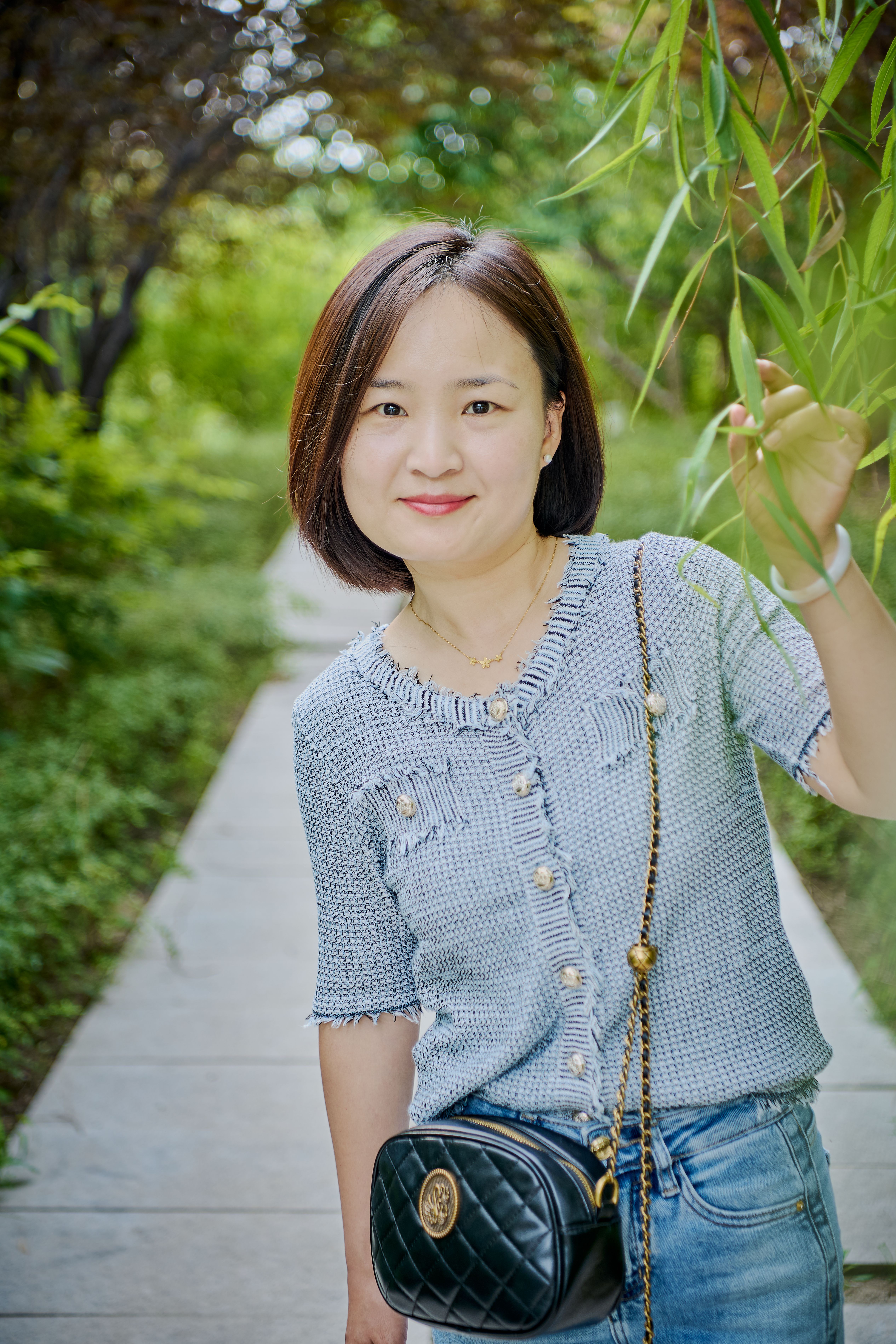 A woman smiling outdoors in a casual outfit, enjoying a peaceful walk in nature.