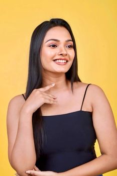 Portrait of a smiling woman in a black dress against a vibrant yellow backdrop