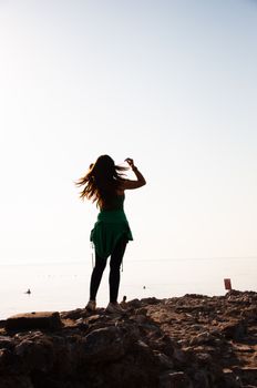 Silhouetted woman stands on a rocky beach at sunset, enjoying the view.