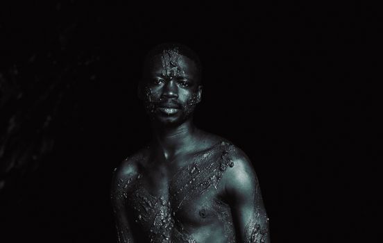 Striking portrait of a man with black body paint on textured skin, set against a dark background.