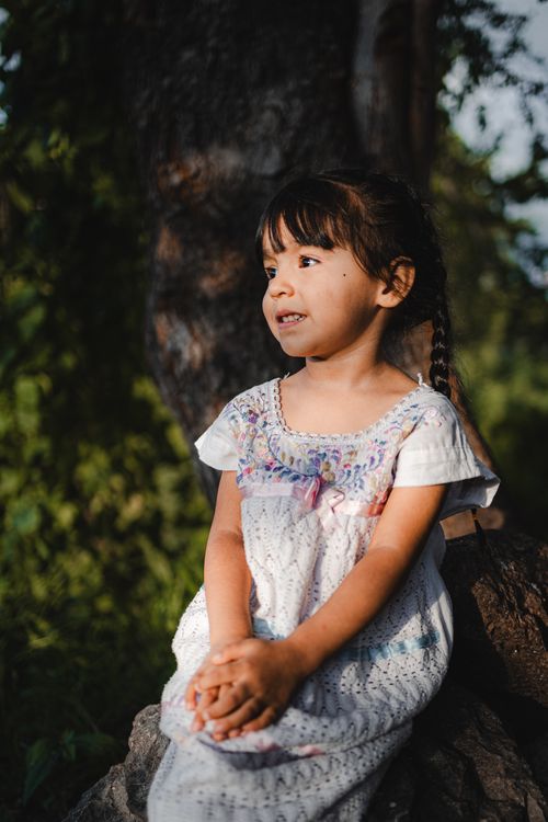 Free A young girl in a white dress sitting outdoors, enjoying the natural setting in Guadalajara, Mexico. Stock Photo