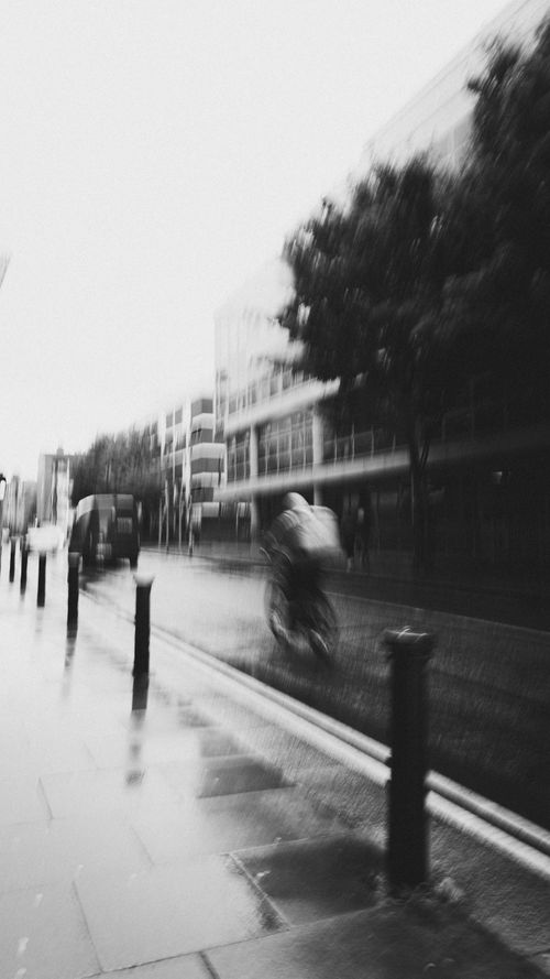 Free Artistic black and white image capturing motion of a cyclist on a rainy city street. Stock Photo