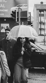 Monochrome photo of people walking with umbrella on rainy urban street.