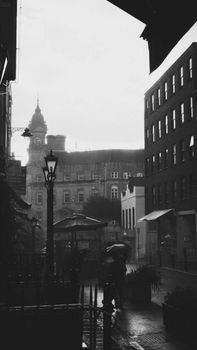 Atmospheric street view in monochrome featuring a clock tower and people under umbrellas.