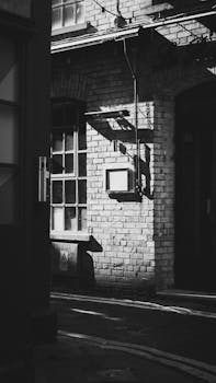 Moody black and white photo of a sunlit urban alleyway with brick architecture.