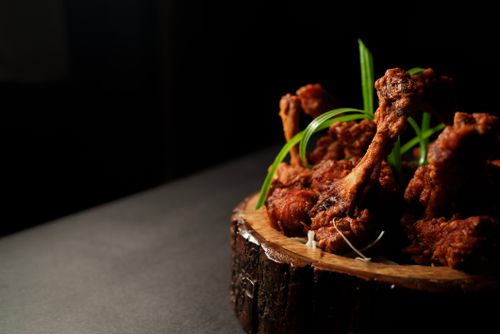 Free Golden brown fried chicken drumsticks garnished with green onions on a wooden platter in dramatic lighting. Stock Photo