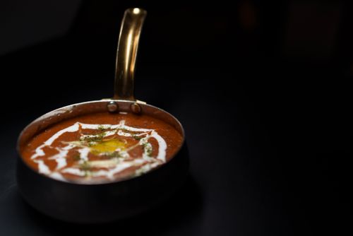 Free Creamy Dal Makhani garnished with herbs and yogurt served in a brass pan on a dark background. Stock Photo