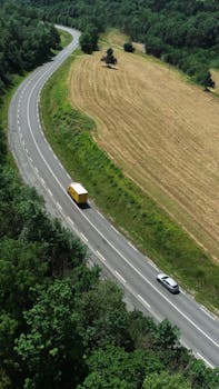 Aerial view of a winding countryside road with cars driving through lush greenery.