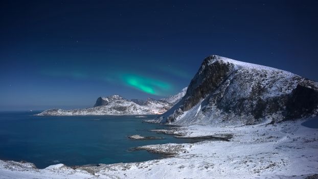 Stunning aurora borealis over a snow-covered coastal landscape at night.