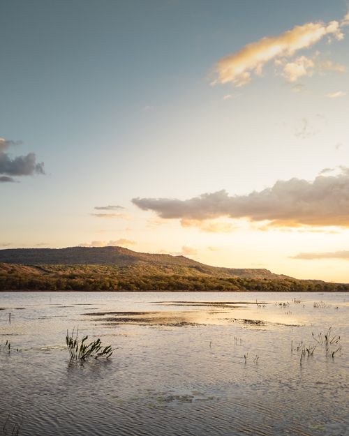 Free A peaceful view of a Brazilian lake at sunset, featuring distant mountains under a cloudy sky. Stock Photo