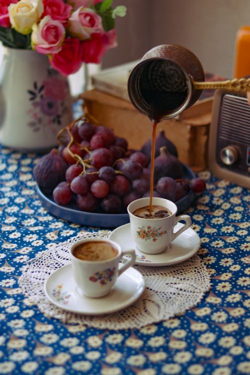 Free Turkish coffee being poured into cups with grapes on a floral tablecloth setting. Stock Photo