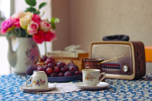 Cozy vintage breakfast scene with flowers, grapes, cups, and a retro radio.