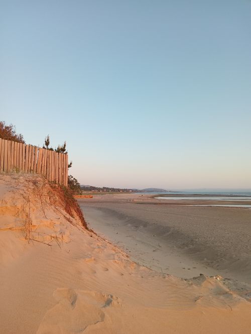 Free A serene beach scene with a wooden fence and calm waves during sunset. Stock Photo