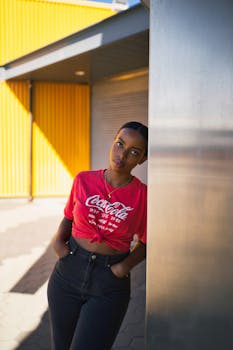 一位时尚女性身着红色上衣，在阳光明媚的城市环境中随意斜倚的肖像