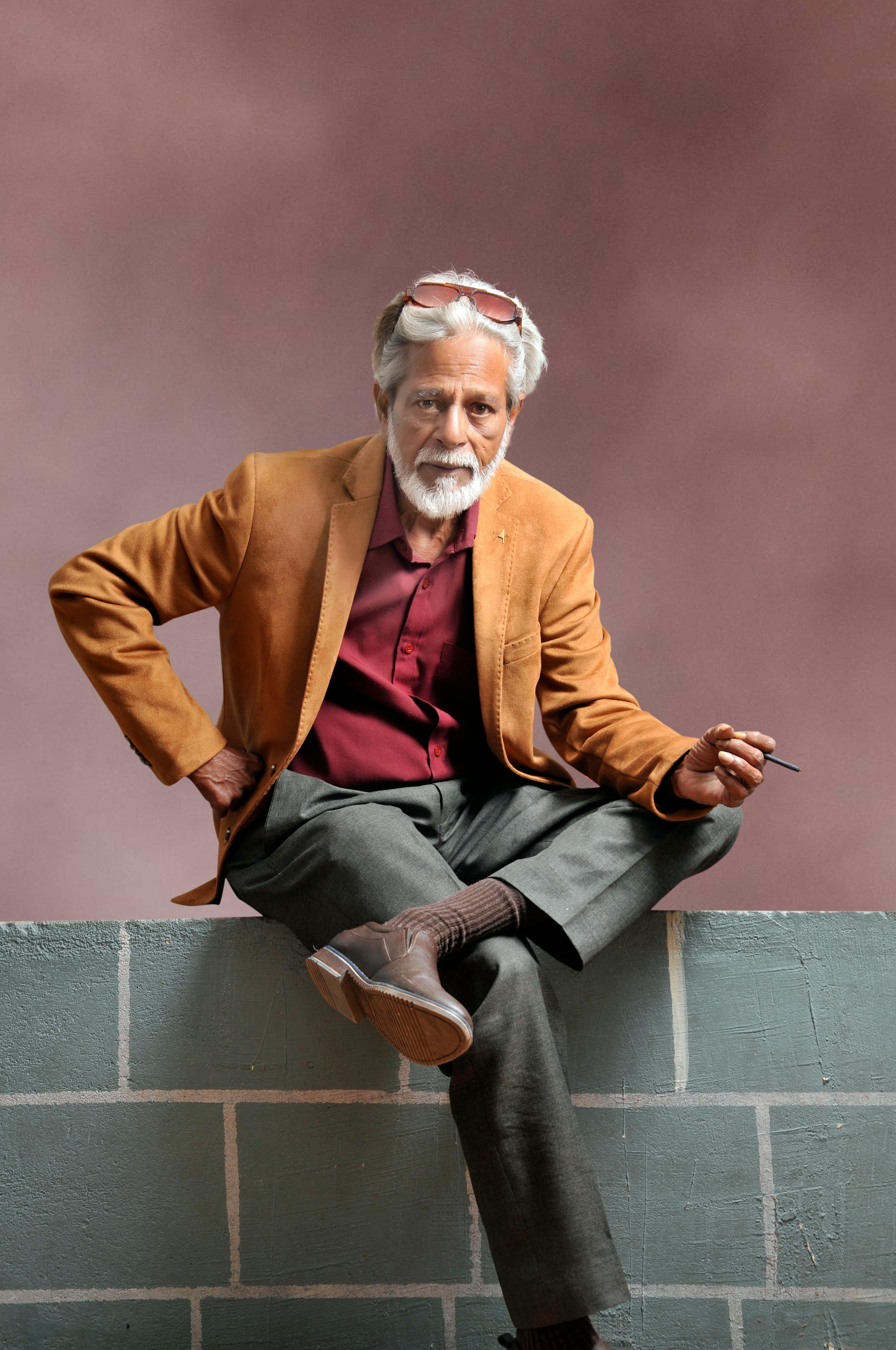 Elegant elderly man seated on a brick wall, exuding confidence and style with vibrant attire.