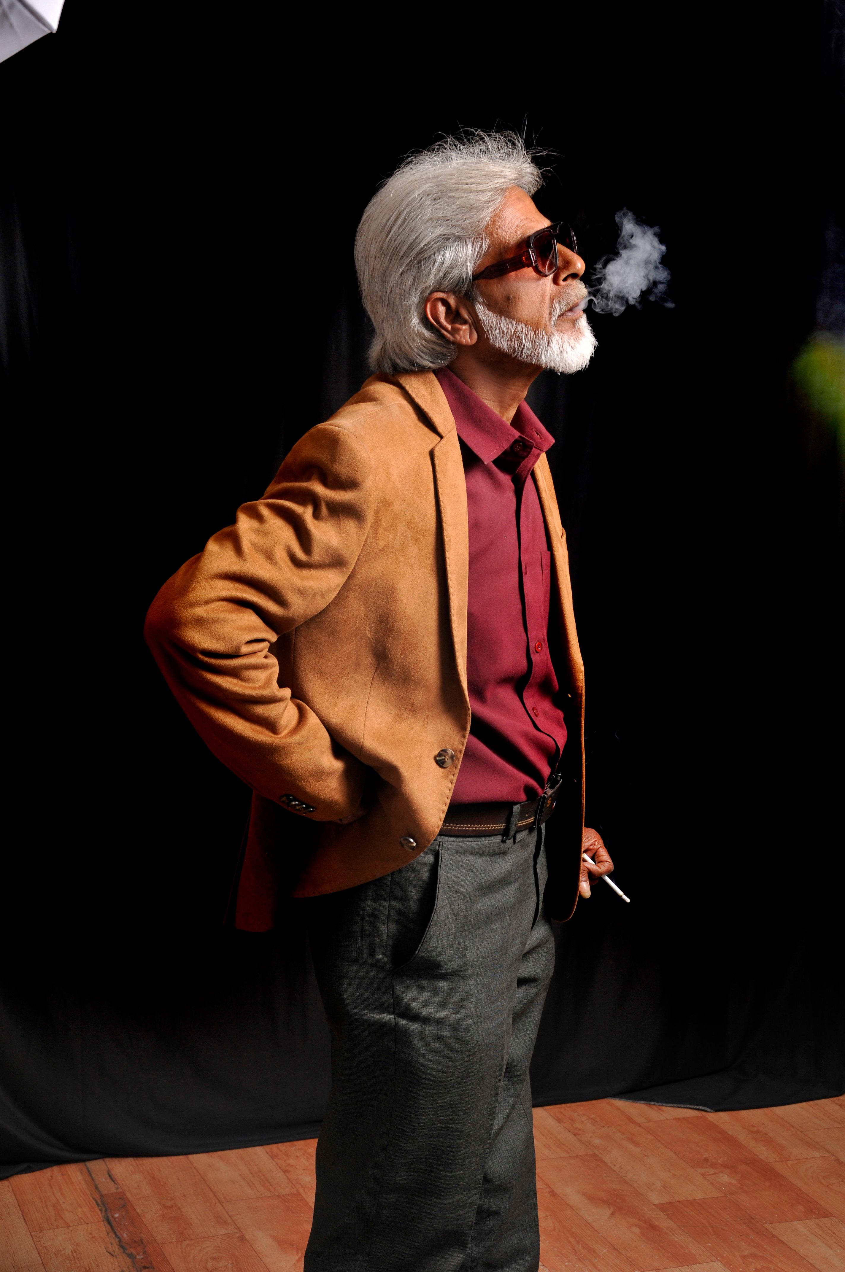 Senior man with sunglasses smoking indoors, exuding style and confidence.