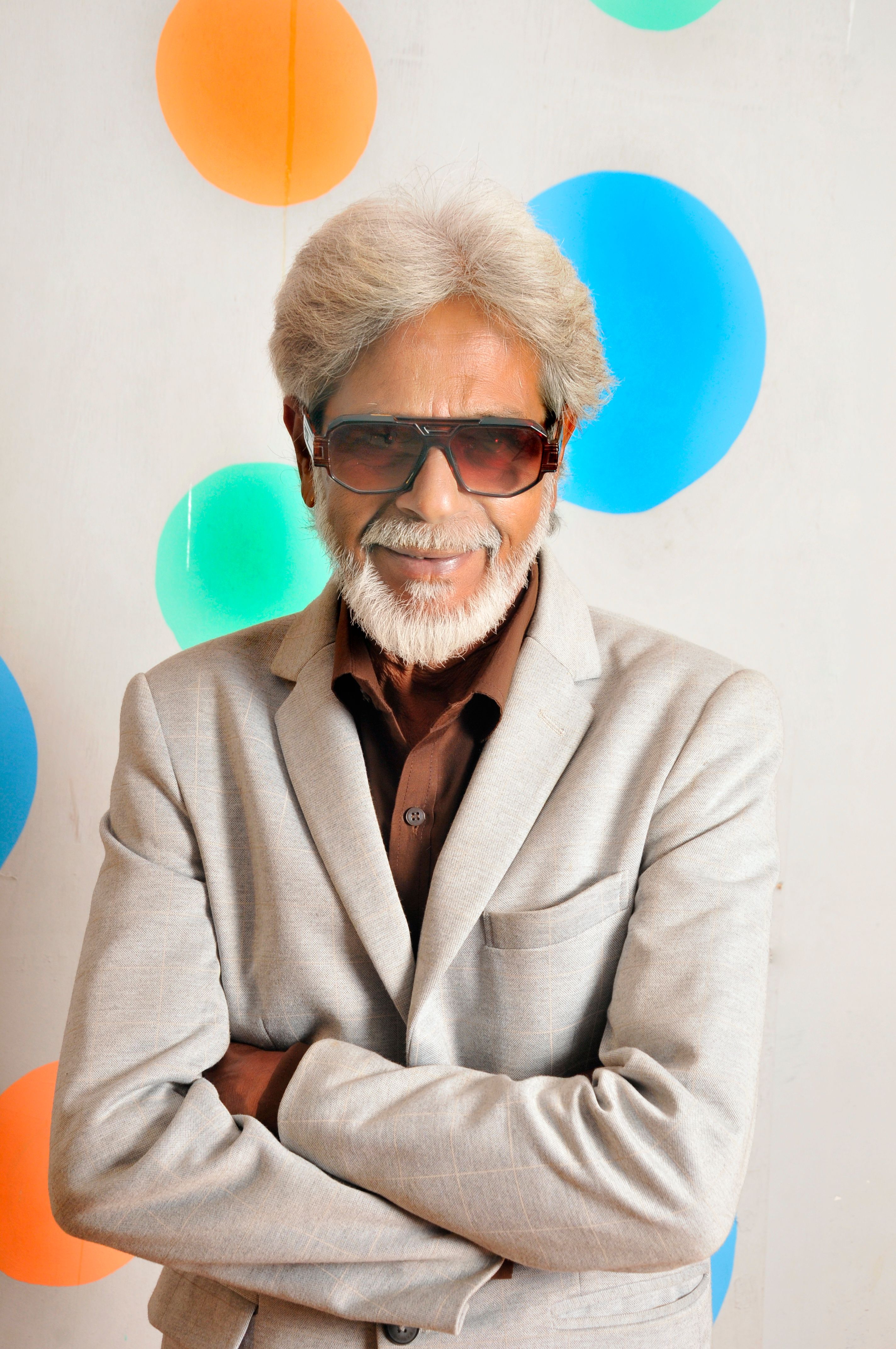 Confident senior man in suit with sunglasses, standing against a vibrant, colorful backdrop.
