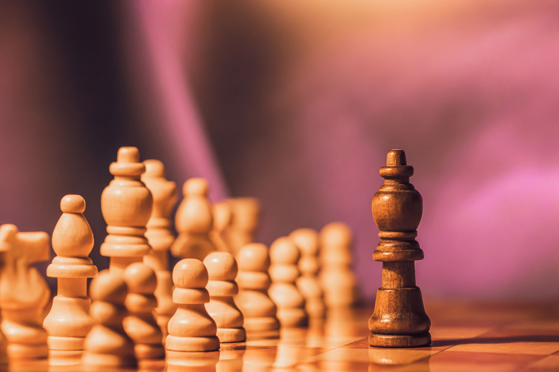 Close-up of wooden chess pieces on a board against a blurred purple backdrop.