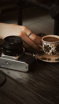 Hand reaching for Turkish coffee in İznik café alongside vintage camera on wooden table.