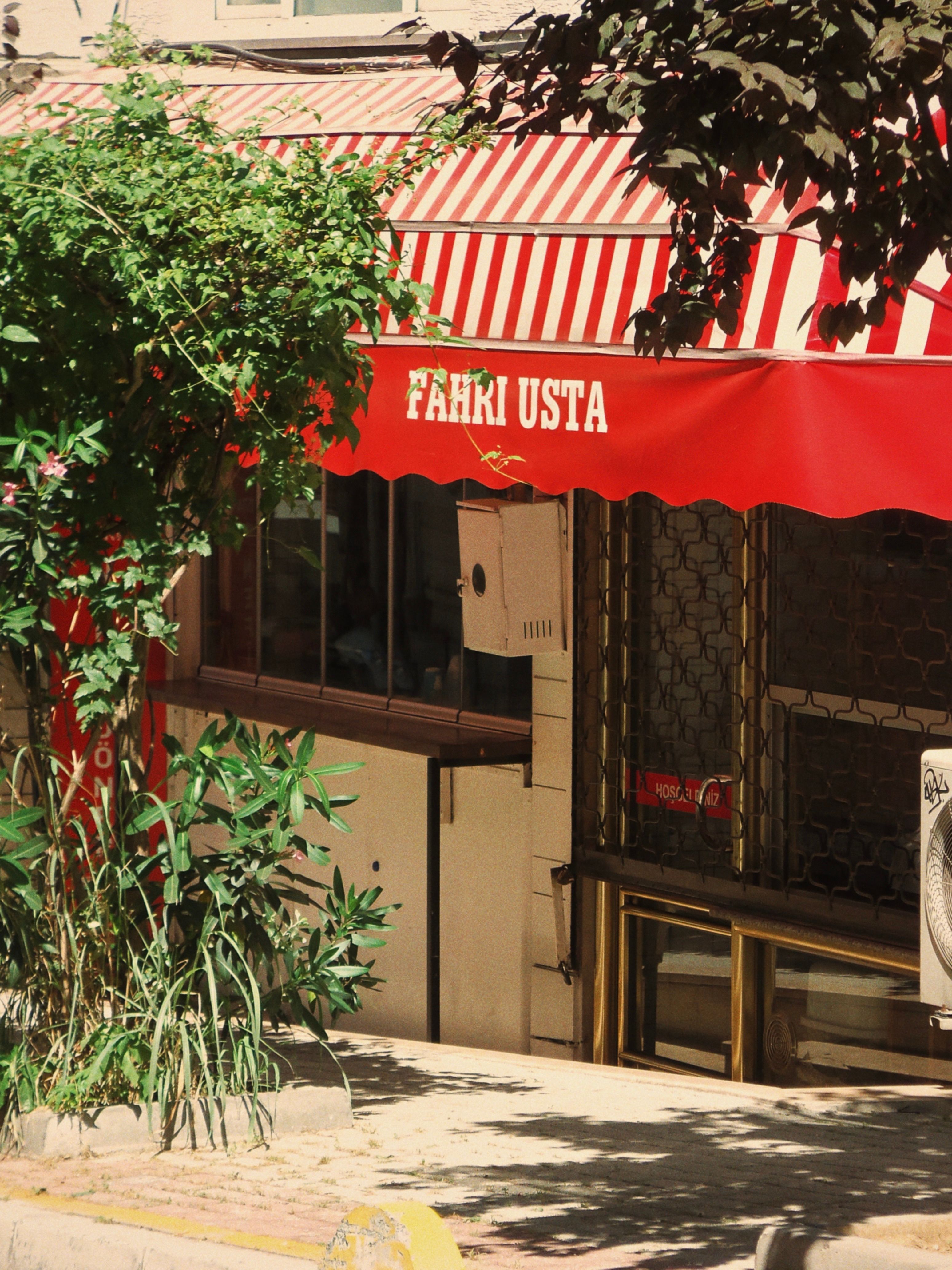 Cozy street café with red striped awning and lush greenery on a sunny day.