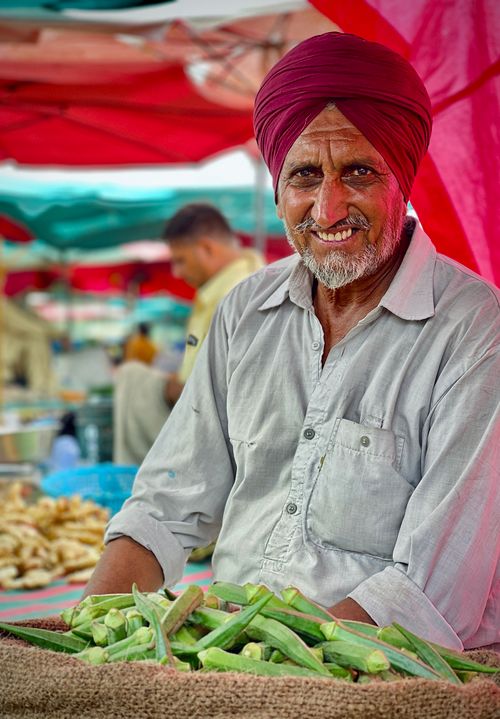 Free Elderly farmer in a vibrant market setting with fresh okra. Colorful and lively atmosphere. Stock Photo