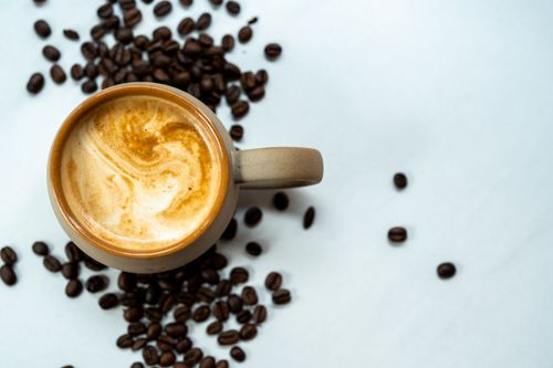 Free A top view of a coffee cup with frothy surface surrounded by roasted coffee beans. Stock Photo