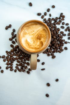 Top-down view of a cappuccino cup with coffee beans on a marble background.