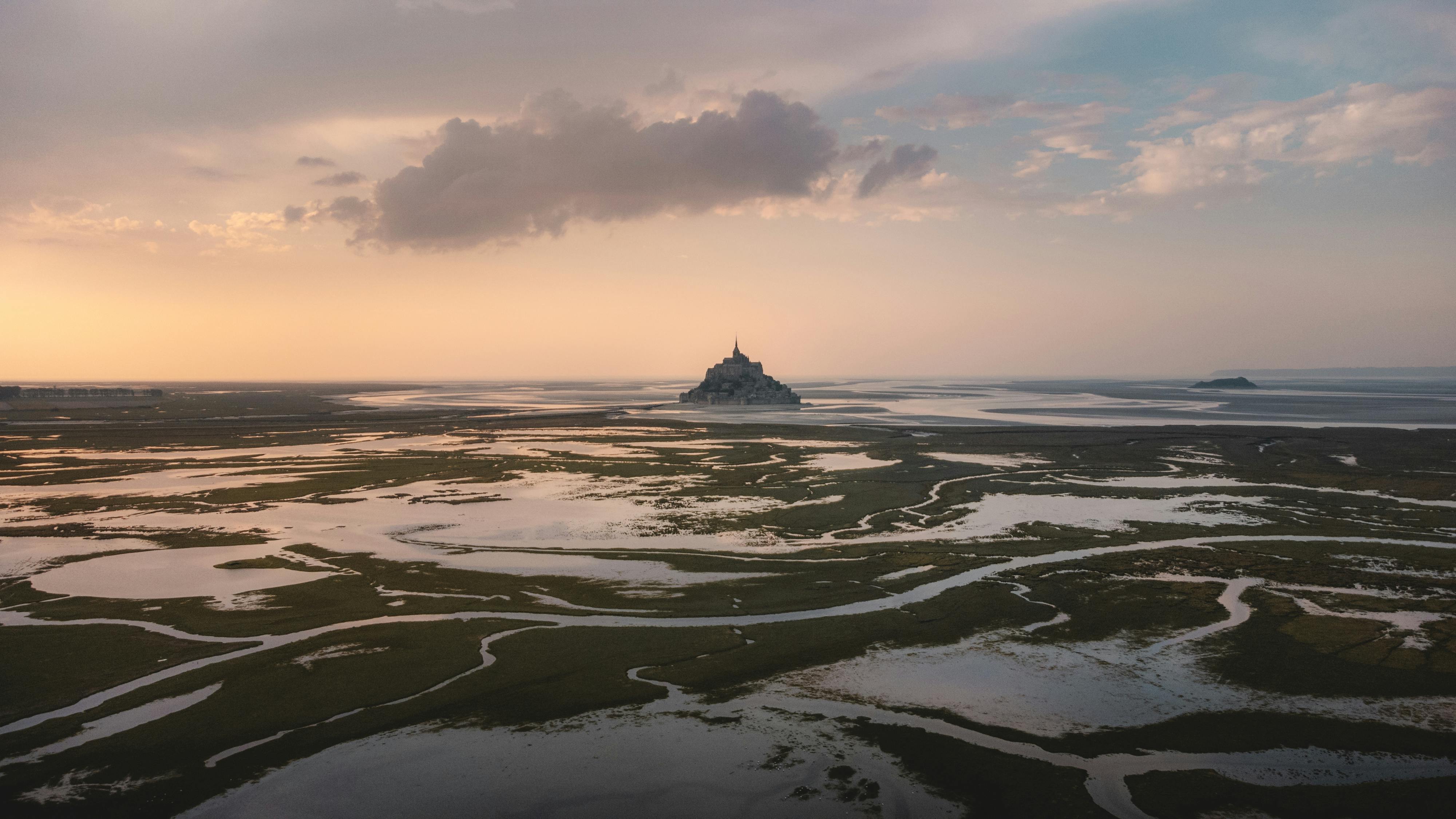 Stunning aerial view of Le Mont-Saint-Michel during low tide at sunset with reflective marshlands.