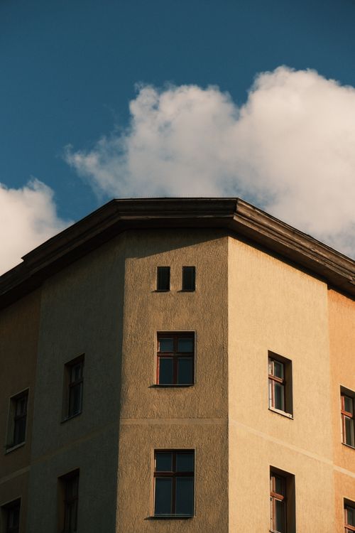 Free Corner of a building captured against a vibrant blue sky with clouds, showcasing architectural details. Stock Photo