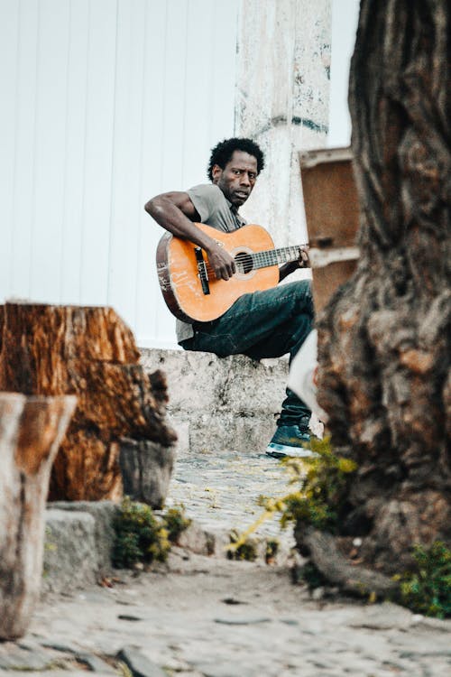 Photo of a Man Sitting on a Stone Playing Guitar