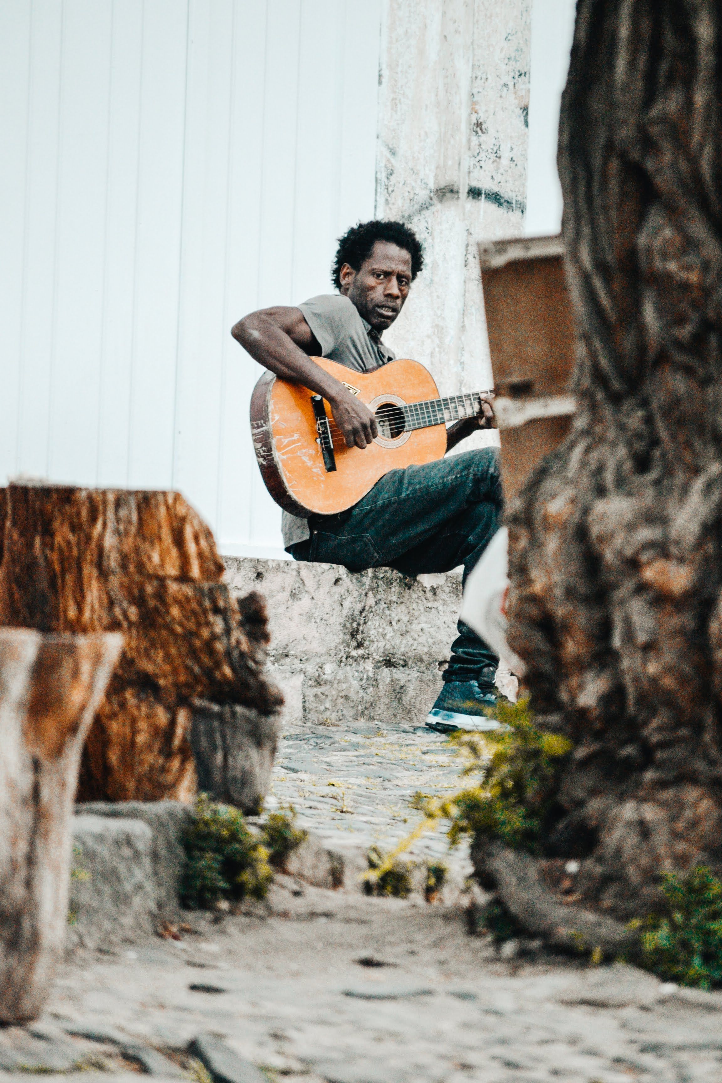 Photo of a Man Sitting on a Stone Playing Guitar · Free Stock Photo