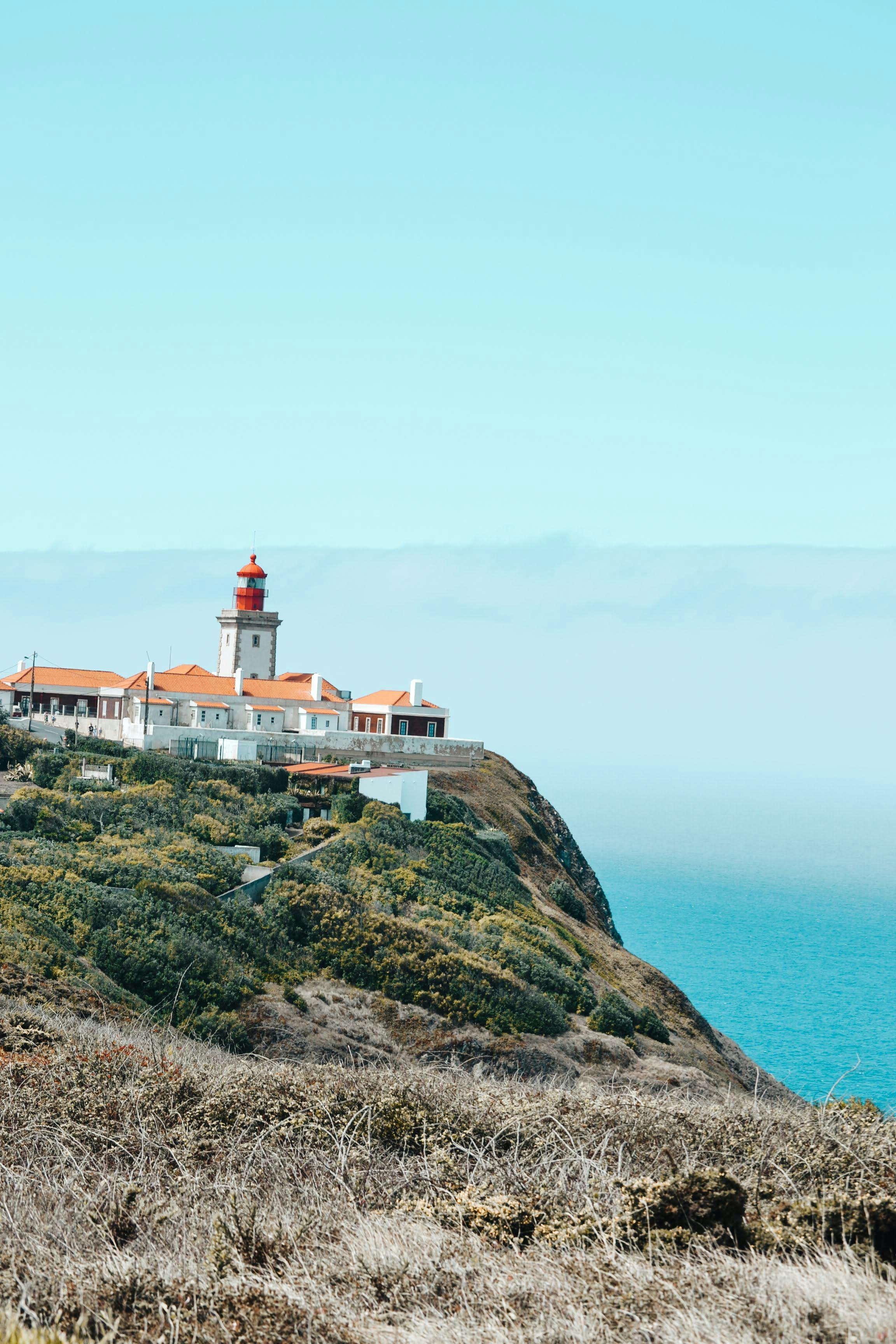 Breathtaking view of a lighthouse atop Portugal's cliff, overlooking the ocean.
