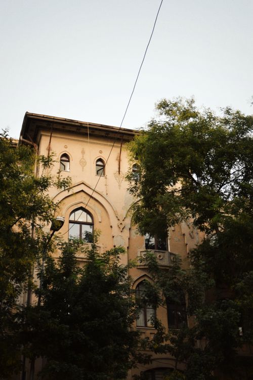 Free Charming historic building facade with arched windows amid green trees, exuding elegance and timeless architectural beauty. Stock Photo