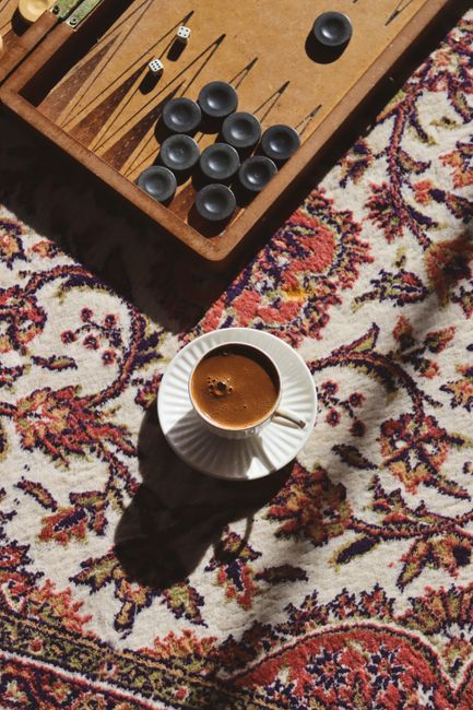 Elegant setup of a coffee cup and backgammon game on a vibrant Persian rug, highlighting cozy leisure time.