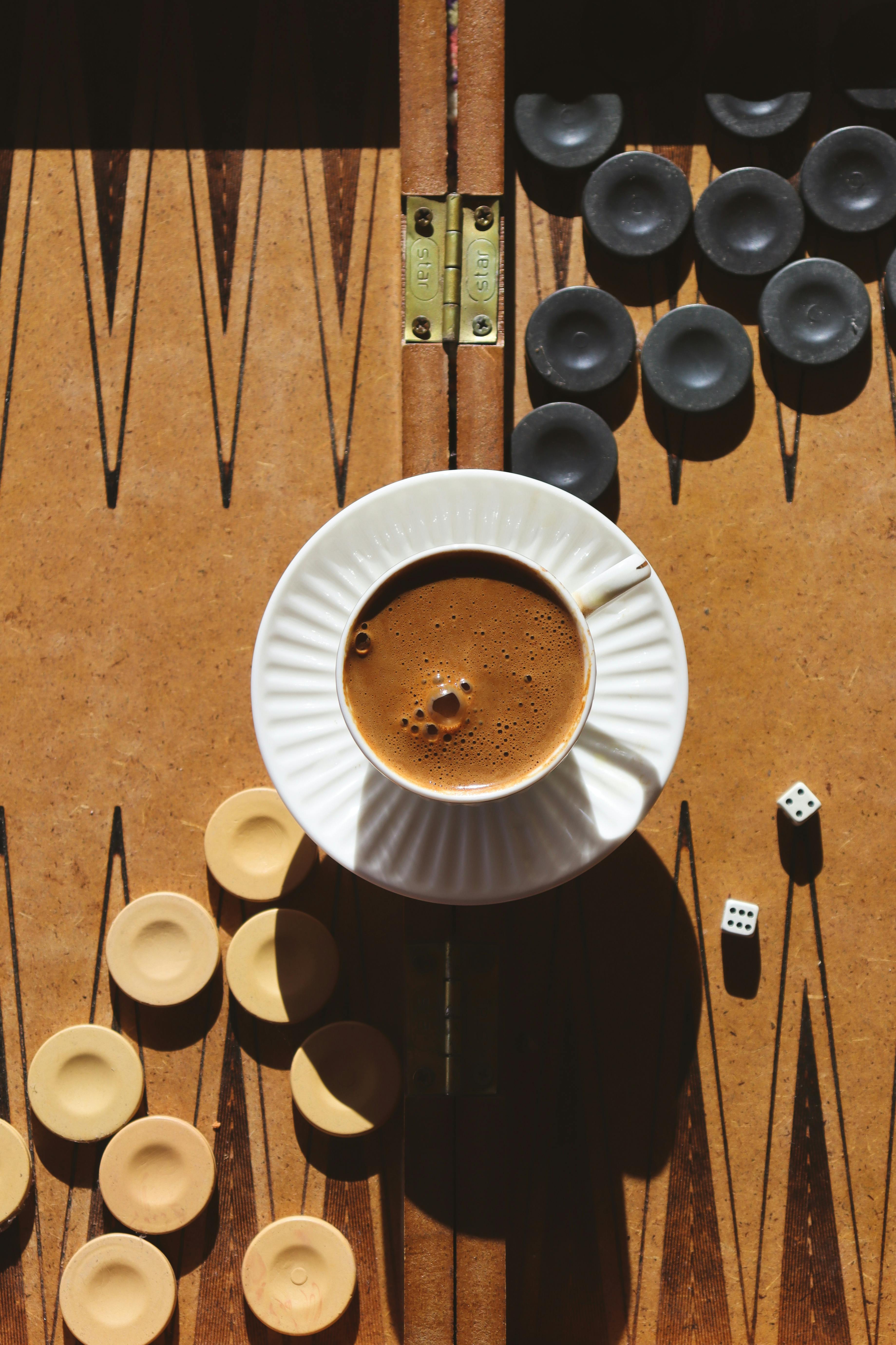 Rustic top view of a cup of coffee on a backgammon board with pieces and dice.